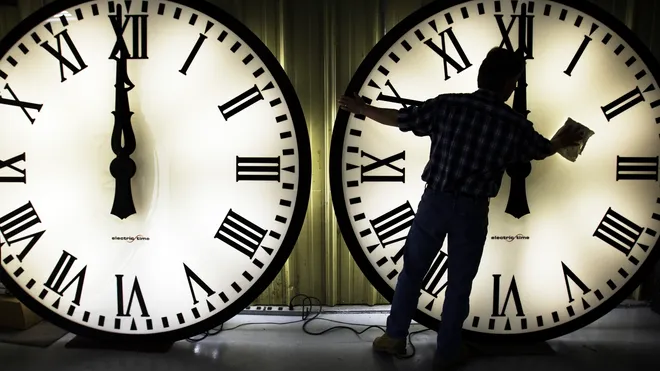 Person adjusting large illuminated clock faces.